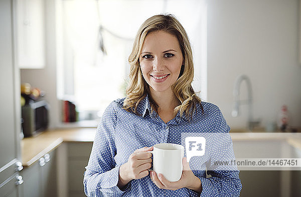 Porträt einer lächelnden Frau  die zu Hause eine Tasse Kaffee hält