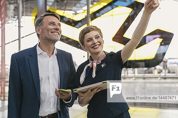 Lächelnder Fluglinienangestellter mit Tablette unterstützt Geschäftsmann am Flughafen