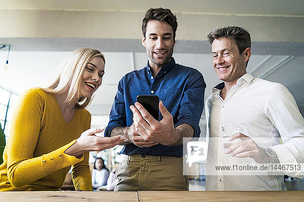 Happy business team looking at cell phone together in loft office