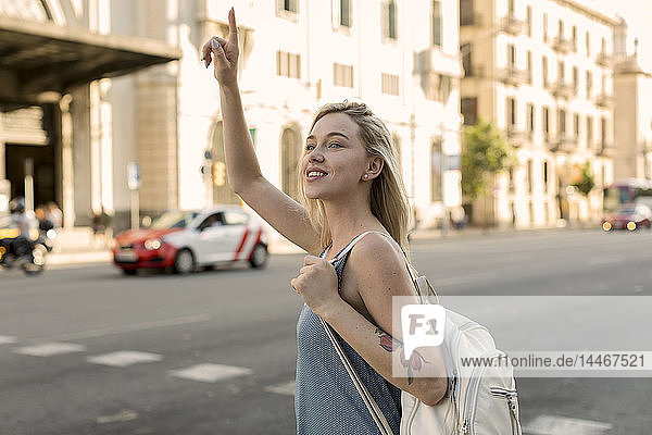 Smiling young woman in the city hailing a taxi