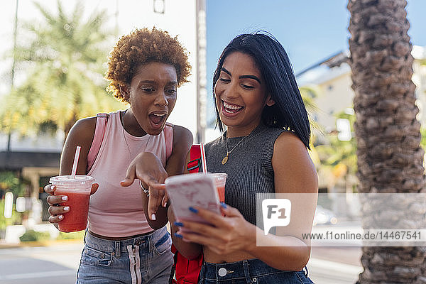 USA  Florida  Miami Beach  zwei glückliche Freundinnen mit Handy und Erfrischungsgetränk in der Stadt