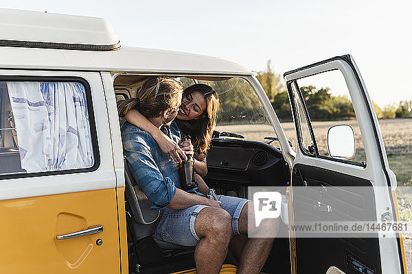 Glückliches Paar sitzt in seinem Wohnwagen  umarmt sich und trinkt ein Getränk