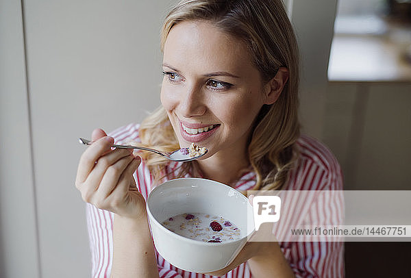 Lächelnde Frau frühstückt morgens zu Hause