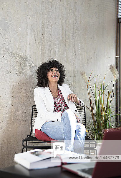 Happy businesswoman sitting on a chair at concrete wall
