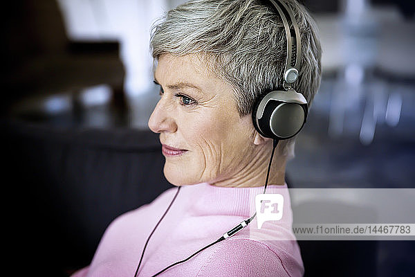 Zufriedene reife Frau  die zu Hause mit Kopfhörern Musik hört