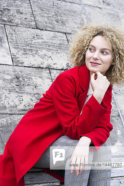 Porträt einer lächelnden blonden Frau mit Ringeln in rotem Mantel  die etwas beobachtet