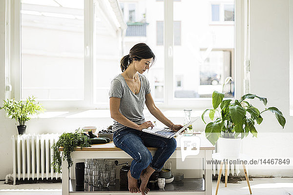 Woman sitting on kitchen table  searching for healthy recipes  using laptop