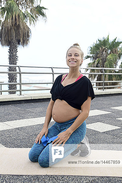 Porträt einer lächelnden schwangeren Frau  die im Freien auf einer Gymnastikmatte kniet