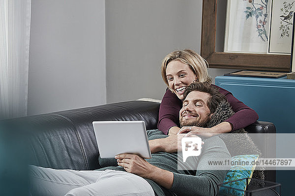 Happy couple with tablet on couch at home