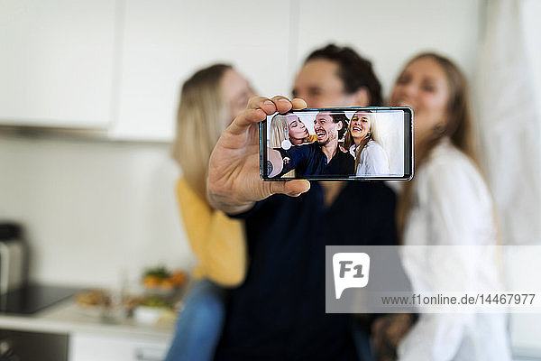 Friends having fun standing in the kitchen  taking pictures with their smartphones