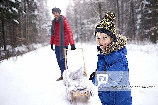 Portrait of smiling little boy in winter with his father and sledge