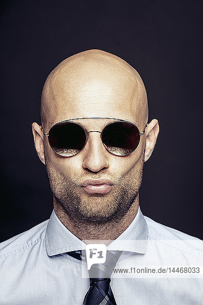 Porträt eines kahlköpfigen Geschäftsmannes mit verspiegelter Sonnenbrille und Schmollmund