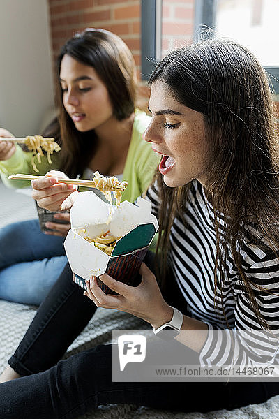 Zwei junge Frauen essen zu Hause asiatisches Essen zum Mitnehmen