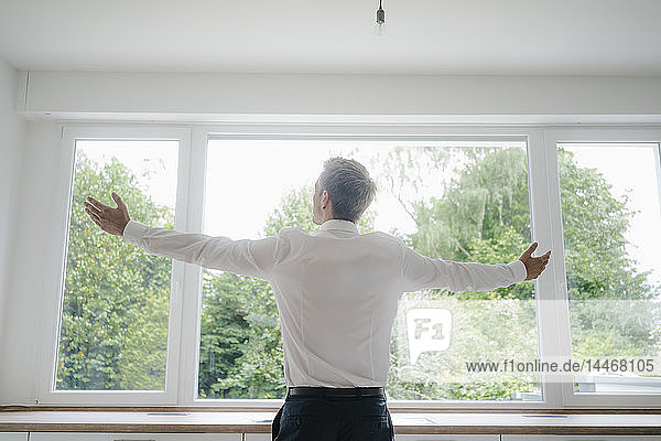 Businessman looking out of the kitchen window of his new home  with arms outstretched
