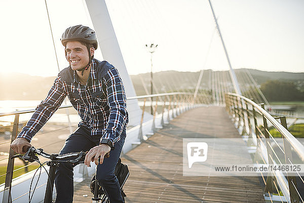 Young man riding bicycle on a bridge at sunset