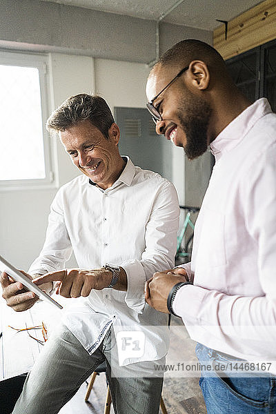 Two smiling businessmen with tablets having a meeting in loft office