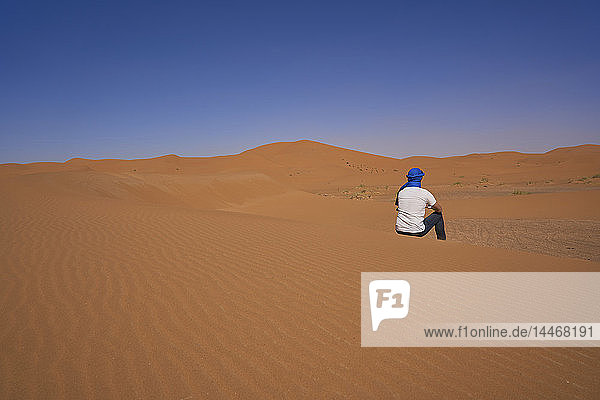 Morocco  back view of man sitting on desert dune