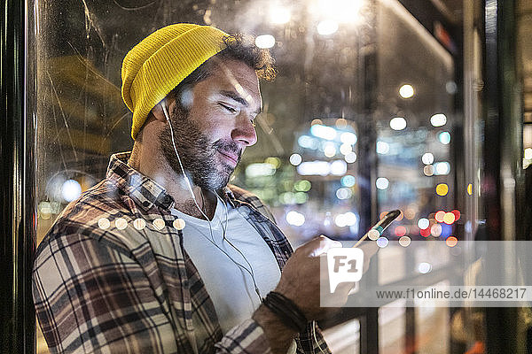 Großbritannien  London  lächelnder Mann an der Bushaltestelle  der auf sein Telefon schaut