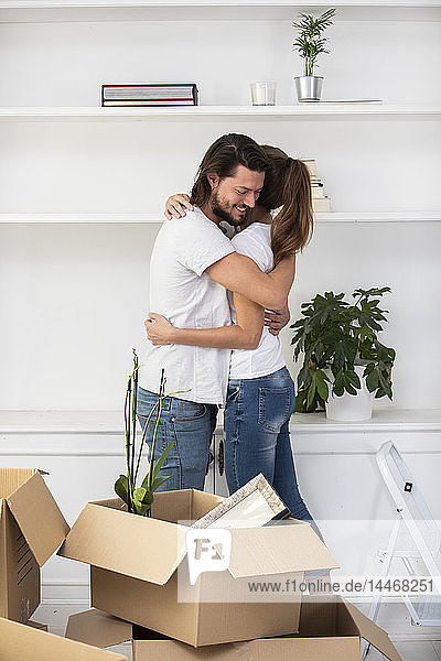 Paar mit Pappkartons umarmt sich im neuen Zuhause