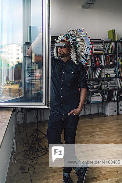 Man wearing Indian headdress and VR glasses in office  looking out of window