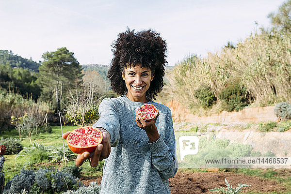 Frau hält halbierten Granatapfel in einer Obstplantage