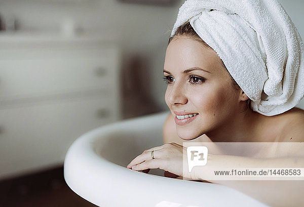 Lächelnde Frau mit Handtuch um den Kopf  die zu Hause ein Bad nimmt