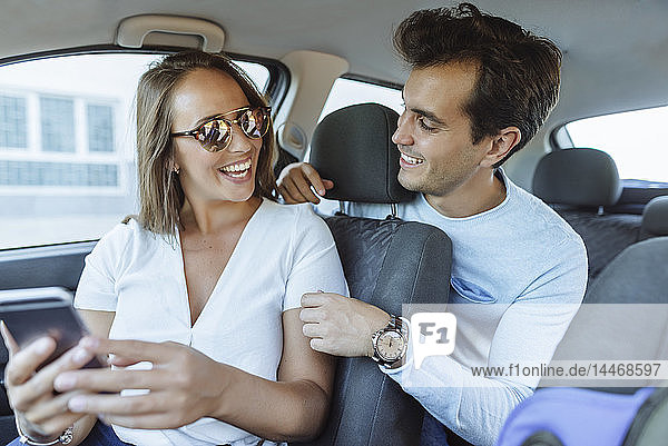 Happy couple in car with man on back seat and woman with cell phone on front passenger seat