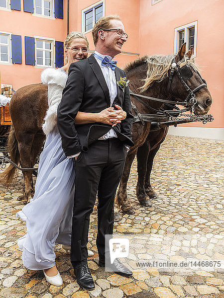 Glückliche Braut und Bräutigam auf Kopfsteinpflasterplatz mit Kutsche