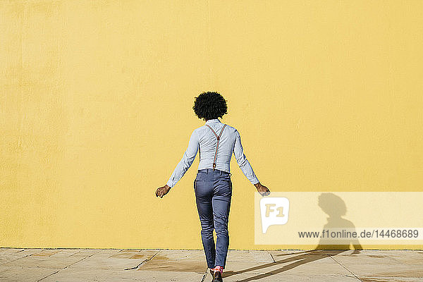 Rückenansicht eines Mannes mit Hosenträgern  der vor der gelben Wand tanzt