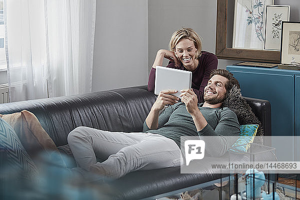 Glückliches Paar mit Tablette auf der Couch zu Hause