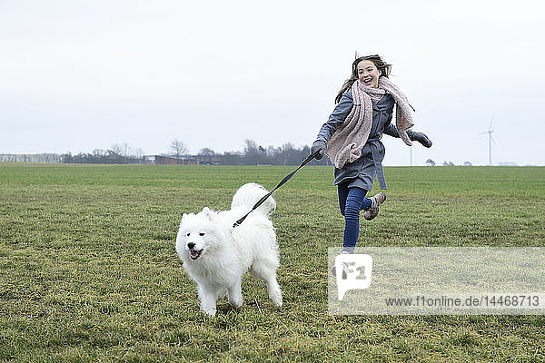 Lachendes Mädchen rennt mit ihrem Hund auf einer Wiese