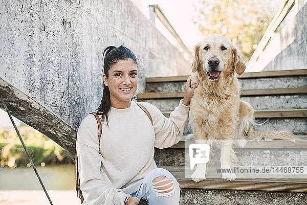 Porträt einer lächelnden jungen Frau mit ihrem Golden-Retriever-Hund auf einer Treppe im Freien