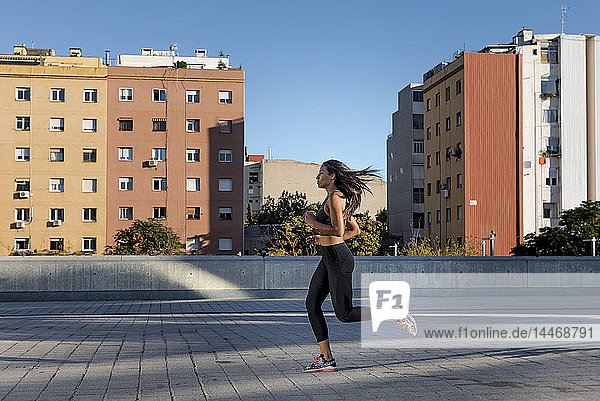 Junge Frau rennt in der Stadt an Wohnblöcken entlang