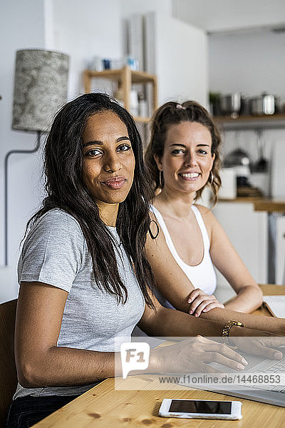 Portrait of two smiling women sitting with laptop at table at home