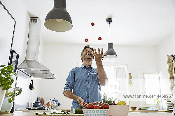 Reifer Mann steht in der Küche und jongliert mit Tomaten