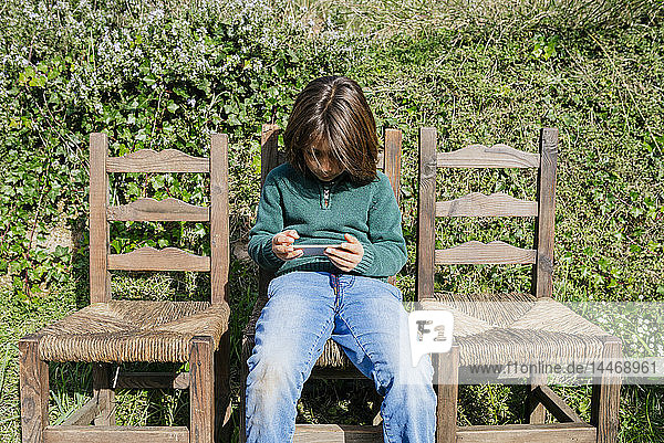 Junge sitzt im Garten und spielt Spiele auf seinem Smartphone