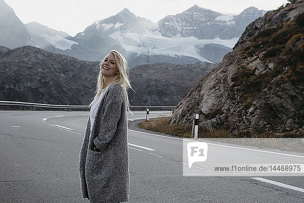 Schweiz  Engadin  glückliche junge Frau steht am Strassenrand in einer Berglandschaft