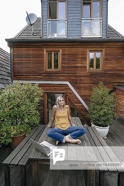Frau entspannt sich auf einem Gartentisch im Hinterhof ihres Hauses
