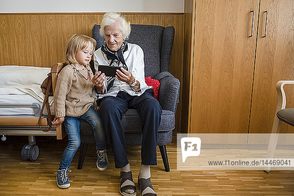 Ältere Frau sieht zusammen mit ihrer Urenkelin Fotos auf Smartphone