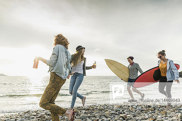 Happy friends with surfboards walking on stony beach