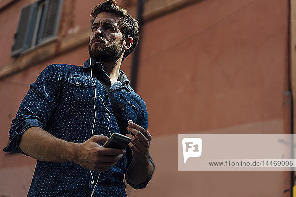 Porträt eines Geschäftsmannes  der Smartphone und Kopfhörer im Freien benutzt