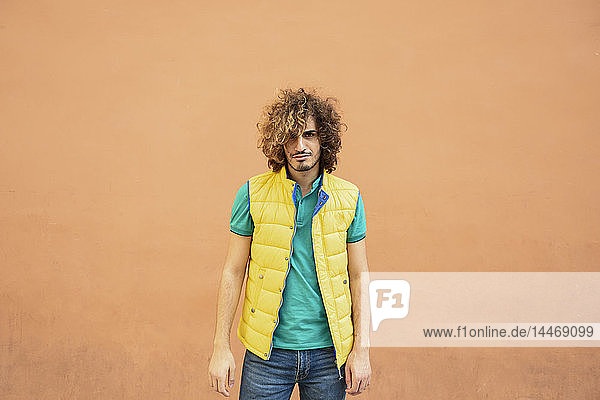 Portrait of annoyed young man with curly hair wearing yellow waistcoat outdoors