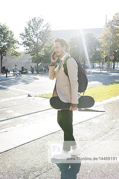 Mann am Telefon mit Rucksack und Skateboard in der Stadt