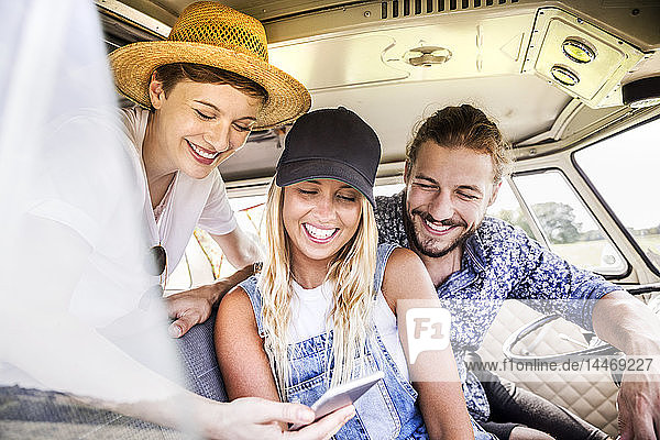 Glückliche Freunde im Lieferwagen schauen auf Smartphone