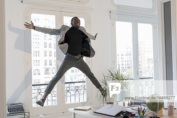 Glücklicher junger Geschäftsmann springt in seinem Büro in die Luft