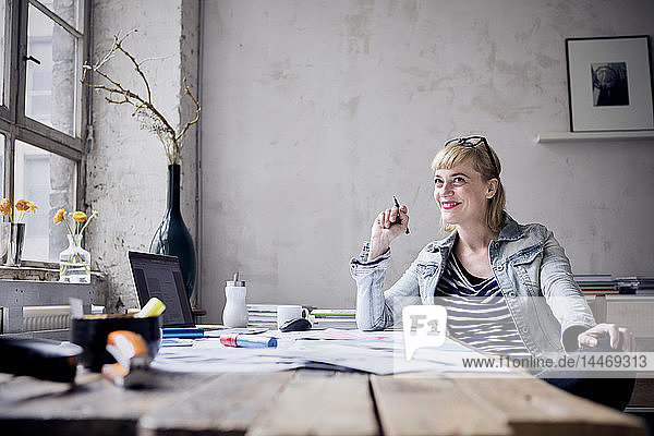 Porträt einer lachenden Frau  die am Schreibtisch in einem Loft sitzt