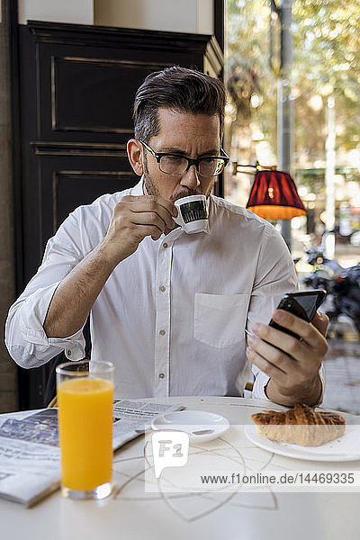 Geschäftsmann frühstückt in einem Cafe und überprüft sein Handy