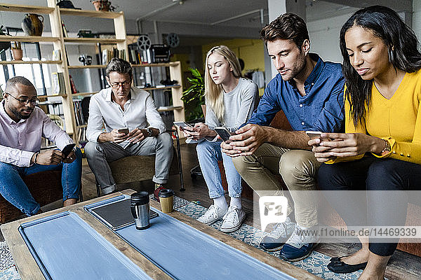 Business team sitting in loft office using cell phones