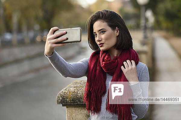 Porträt einer jungen Frau mit rotem Schal  die sich mit dem Handy selbstständig macht