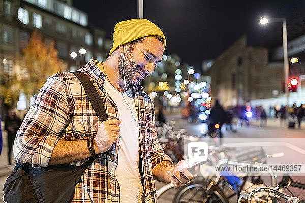 Großbritannien  London  Mann  der nachts in der Stadt pendelt und auf sein Telefon schaut